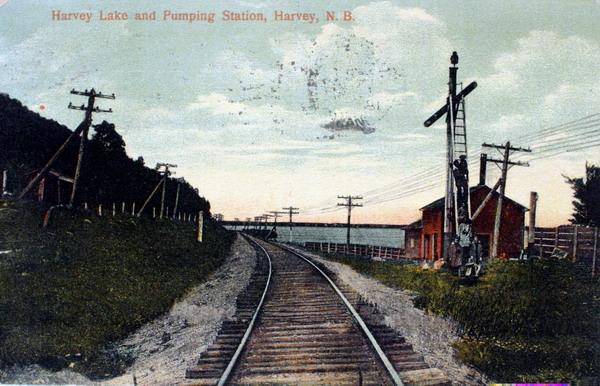 Postcard of &#039;Harvey Lake and Pumping Station, Harvey, N.B&#039;. Several people posing on ladder used by section men to service steam cars with water drawn from Harvey Lake, this structure is no longer present.Photographed around 1910. Image thanks to J. Hall.
